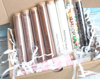 May include: A cardboard box filled with clear glass test tubes containing different types of chocolate and sprinkles. The tubes are labeled "Milk Chocolate", "Marshmallow", "Dark Chocolate", "White Chocolate", and "White Chocolate".