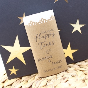 May include: A brown paper wrapped tissue packet with a white tissue inside. The packet has a white lace trim and the text "For Your Happy Tears" in black cursive font. Below the text is the couple's names "Jazmine & James" and the date "18th August 2020".