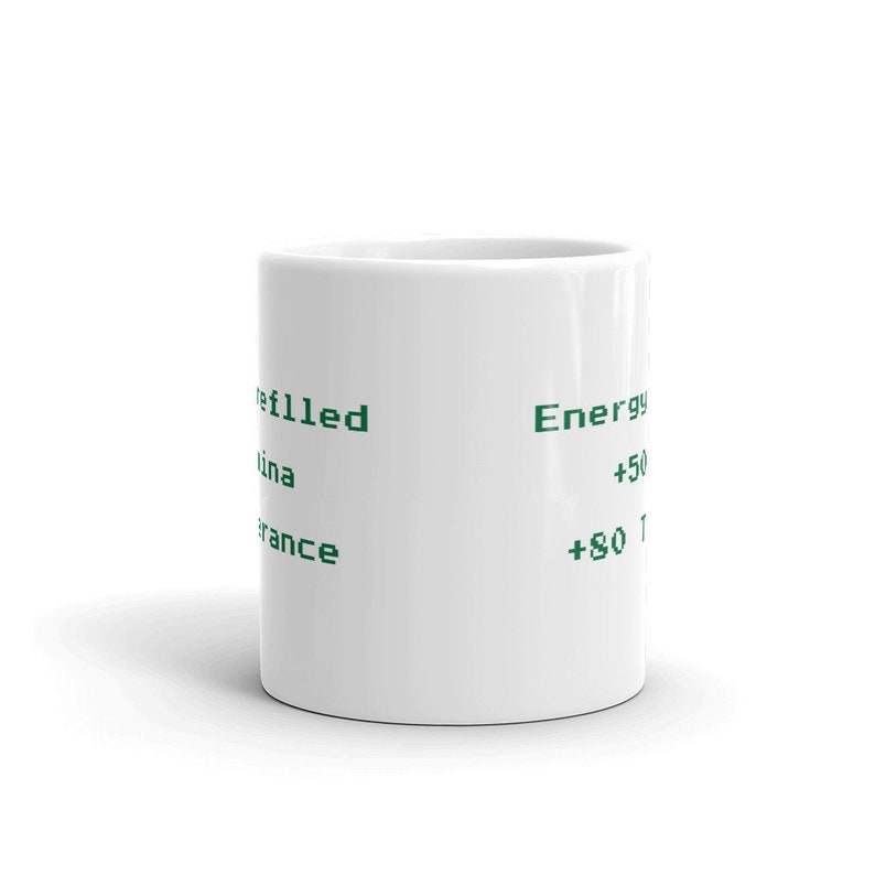 May include: A white ceramic coffee mug with green text. The text includes the words "refilled", "Energy", and phone numbers. The mug is cylindrical and sits on a white surface.
