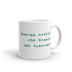 May include: White ceramic mug with green text that reads "Energy refilled", "+50 Stamina", and "+80 Tolerance". The mug has a curved handle and a glossy finish. A perfect gift for gamers.