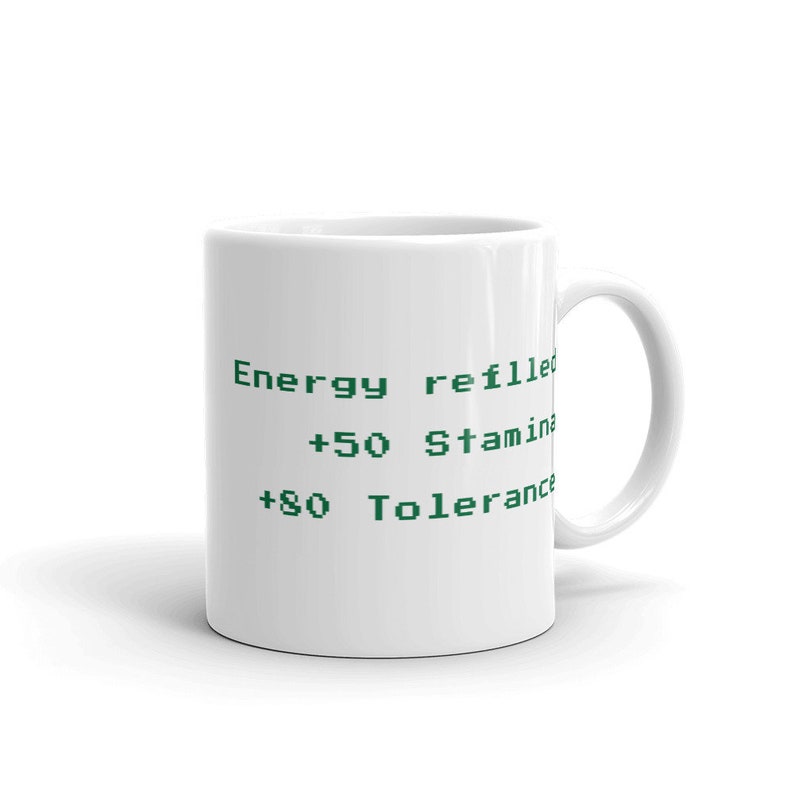 May include: White ceramic mug with green text that reads "Energy refilled", "+50 Stamina", and "+80 Tolerance". The mug has a curved handle and a glossy finish. A perfect gift for gamers.