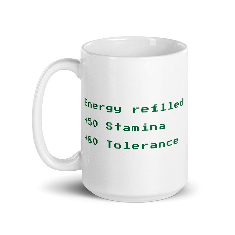 May include: White ceramic mug with a curved handle. The mug features green text that reads "Energy refilled, +50 Stamina, +80 Tolerance". The mug is designed for hot or cold beverages.