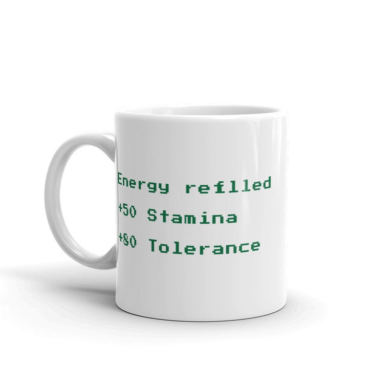 May include: White ceramic mug with a curved handle. The mug features green text that reads "Energy refilled", "+50 Stamina", and "+80 Tolerance". A simple, everyday coffee mug.