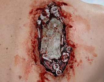 Könnte beinhalten: Nahaufnahme einer blutigen, falschen Wunde auf dem Rücken einer Person. Die Wunde ist mit Metallteilen und Schrauben gefüllt, was einen realistischen und grausamen Effekt erzeugt.