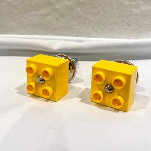 May include: Two yellow plastic drawer pulls shaped like Lego bricks with chrome accents.
