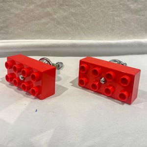 May include: Two red plastic drawer pulls shaped like Lego bricks with silver metal knobs.