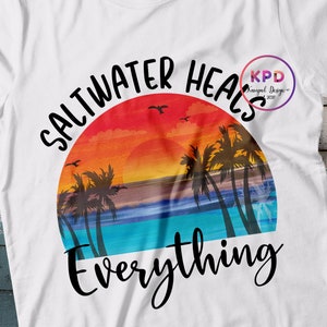 K&ouml;nnte beinhalten: Ein wei&szlig;es T-Shirt mit einem Sonnenuntergangs-Motiv und dem Text "Saltwater heals everything". Das Motiv zeigt Palmen, einen Sonnenuntergang und einen Ozean.