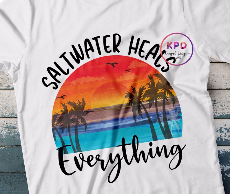 K&ouml;nnte beinhalten: Ein wei&szlig;es T-Shirt mit einem Sonnenuntergangs-Motiv und dem Text "Saltwater heals everything". Das Motiv zeigt Palmen, einen Sonnenuntergang und einen Ozean.