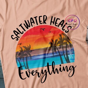 K&ouml;nnte beinhalten: Ein pfirsichfarbenes T-Shirt mit einem Sonnenuntergangs-Motiv und dem Text "Saltwater Heals Everything".