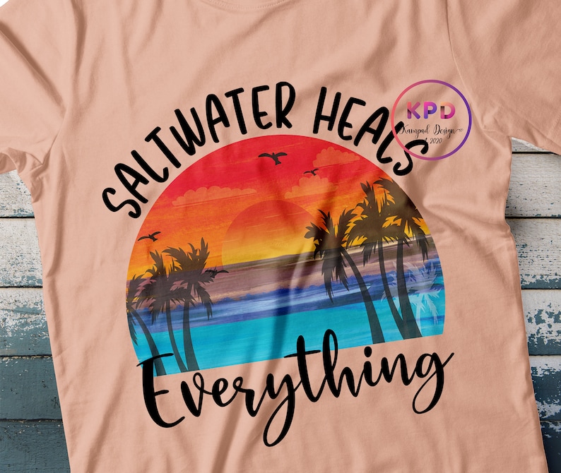 K&ouml;nnte beinhalten: Ein pfirsichfarbenes T-Shirt mit einem Sonnenuntergangs-Motiv und dem Text "Saltwater Heals Everything".