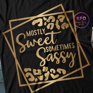 Puede incluir: Camiseta negra con un dise&ntilde;o gr&aacute;fico dorado que dice "Mostly Sweet Sometimes Sassy" con detalles de estampado de leopardo.