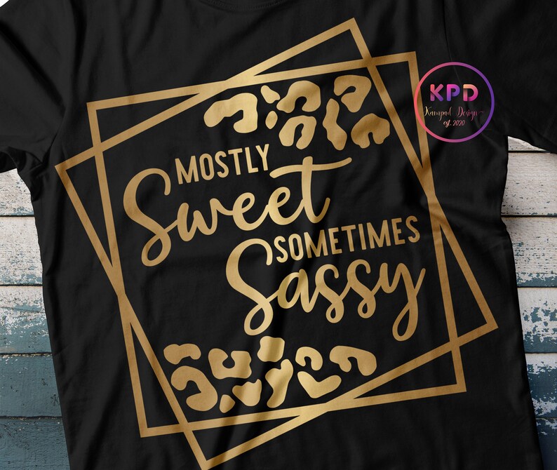 Puede incluir: Camiseta negra con un dise&ntilde;o gr&aacute;fico dorado que dice "Mostly Sweet Sometimes Sassy" con detalles de estampado de leopardo.