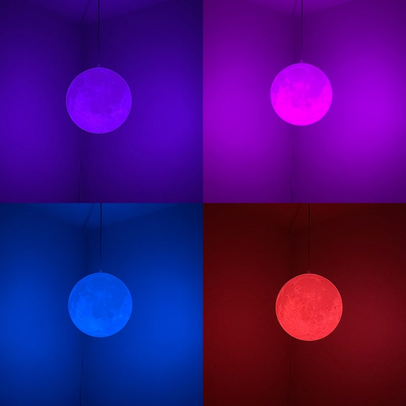 May include: A hanging moon-shaped lamp glows with different colors: purple, pink, blue, and red. The lamp is suspended from a wire and casts a soft light, creating a celestial ambiance. The lamp's surface has a textured, cratered appearance.
