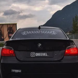 May include: Black BMW sedan with a rear spoiler, red taillights, and a decorative window decal. The car has a license plate with the Instagram handle @QREEUEL. A "CUTNINJA" sticker is visible on the bumper.