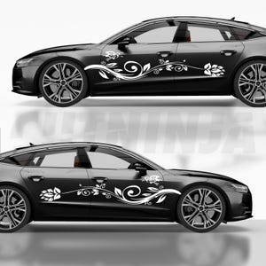 May include: Two black cars with white floral decals on the sides. The decals feature stylized flowers, leaves, and swirling vines. The cars have black rims and tinted windows, and are set against a white background.