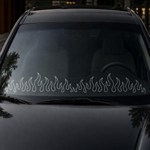 Peut inclure: Un pare-brise de voiture noir avec un autocollant blanc représentant des flammes stylisées disposées horizontalement sur la partie inférieure de la vitre. Le motif se compose de formes de flammes répétitives aux lignes fines.