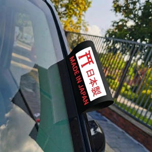 May include: A black sticker with the text "MADE IN JAPAN" in red and white, along with Japanese characters. The sticker is affixed to a car window.