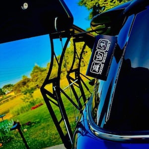 Puede incluir: Primer plano de un coche azul brillante con un alerón negro. Una pequeña pegatina rectangular con las palabras "HAND WASH ONLY" e iconos relacionados está adherida al coche. El fondo muestra un cielo azul brillante y hierba verde.