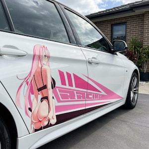 Pode incluir: Um carro branco apresenta um grande adesivo de vinil na porta lateral. O gráfico exibe uma personagem de anime com longos cabelos cor-de-rosa vestindo lingerie preta, ao lado de formas geométricas rosas e a palavra RACING em fonte estilizada.
