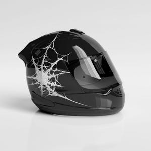 May include: A glossy black motorcycle helmet with a silver spiderweb design on the side. The helmet has a tinted visor and a streamlined shape. The design is a striking contrast against the black surface.