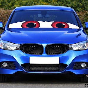 May include: A vibrant blue car with large cartoon eyes on the windshield. The eyes are white with red irises and black pupils. The car has a black grill and a white license plate area. The image is taken outdoors.
