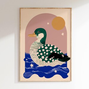 May include: Framed art print depicting a duck with a green head and a body covered in white polka dots. The duck is on blue water, with a pink arch, a yellow sun, and stars. The artwork is in a frame.
