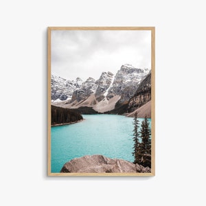 May include: A scenic photograph of a turquoise lake surrounded by snow-capped mountains. The lake is calm and reflects the sky, and there are a few trees in the foreground.