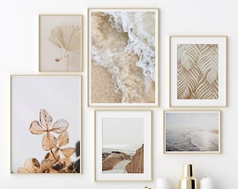 May include: A gallery wall with six framed prints featuring beach scenes, waves, and botanical elements. The prints are arranged in a symmetrical pattern on a white wall. The wall is above a light blue cabinet with gold and white vases.