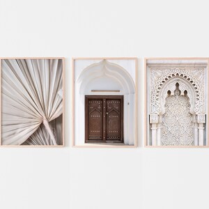 May include: Three framed prints with a minimalist aesthetic. The left print features a close-up of a beige palm leaf. The centre print shows a white archway with a wooden door. The right print shows a white archway with intricate carvings.