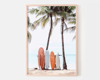 May include: Four surfboards leaning against a wooden rack on a beach with two palm trees in the background. The surfboards are orange, white, and blue.