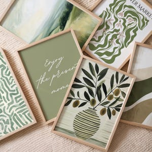 May include: A collection of framed art prints with a natural, botanical theme. The prints feature olive branches in a vase, abstract landscapes, and floral designs in shades of green and beige. One print has the text "Enjoy the present moment".