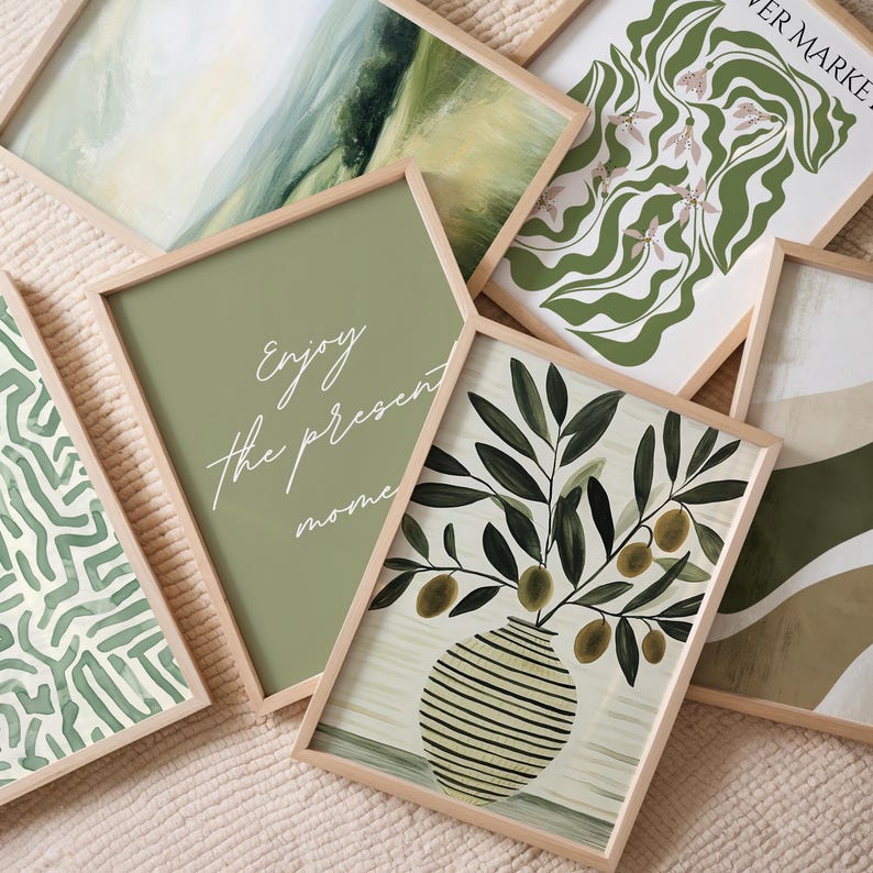 May include: A collection of framed art prints with a natural, botanical theme. The prints feature olive branches in a vase, abstract landscapes, and floral designs in shades of green and beige. One print has the text "Enjoy the present moment".