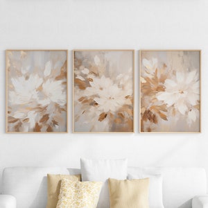May include: A set of three abstract art prints featuring a muted brown and white floral design. The prints are framed in a light wood frame.