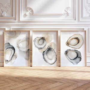 May include: Three framed watercolor prints featuring oyster shell designs in shades of gray, white, and beige. The artwork is displayed against a white wall with decorative molding and a wooden floor.