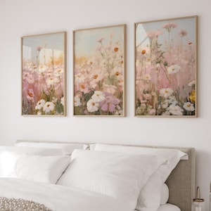 May include: Three framed prints depicting a field of pink and white flowers. The prints are in a light wood frame and are hung on a white wall.