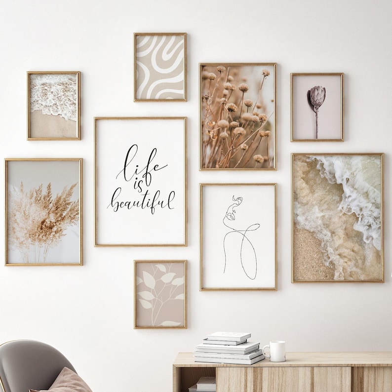May include: A gallery wall with nine framed prints in a neutral colour palette. The prints feature abstract shapes, dried flowers, a line drawing of a face, and beach scenes. The text "life is beautiful" is featured on one of the prints.