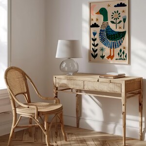Puede incluir: Una impresi&oacute;n art&iacute;stica enmarcada con una ilustraci&oacute;n caprichosa de un pato en verde, azul y naranja. La obra de arte cuelga sobre un escritorio de madera clara con una l&aacute;mpara de cristal y una silla de mimbre. La habitaci&oacute;n tiene una paleta de colores neutros.