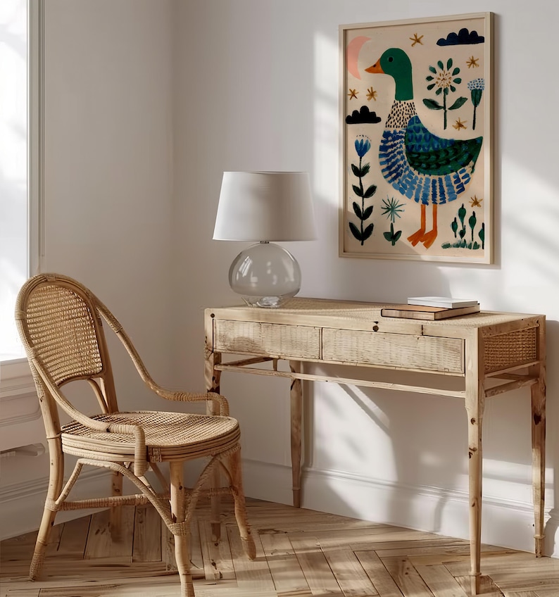 Puede incluir: Una impresi&oacute;n art&iacute;stica enmarcada con una ilustraci&oacute;n caprichosa de un pato en verde, azul y naranja. La obra de arte cuelga sobre un escritorio de madera clara con una l&aacute;mpara de cristal y una silla de mimbre. La habitaci&oacute;n tiene una paleta de colores neutros.