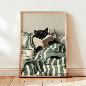 Può includere: Stampa incorniciata con un gatto nero che legge un libro a letto. Il gatto è sotto una coperta a righe verdi e bianche, con una tazza di tè accanto. La stampa ha una cornice in legno chiaro ed è ambientata su uno sfondo neutro.