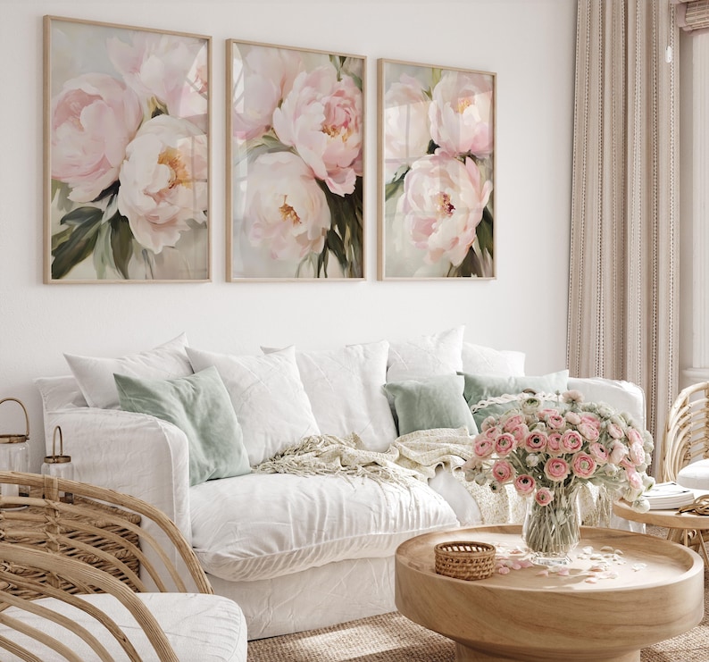 May include: Three framed floral art prints featuring soft pink peonies with green foliage. The artwork hangs above a white sofa with decorative pillows and a wooden coffee table. A vase of pink flowers sits on the table.