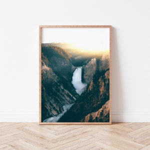May include: A framed photograph of a waterfall cascading down a rocky cliffside, surrounded by lush green trees. The sun is shining brightly in the background, creating a warm glow over the scene.