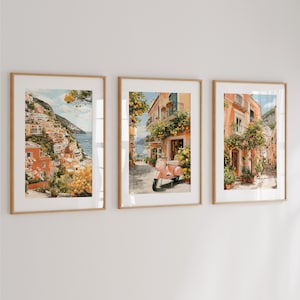 May include: Three framed art prints showcasing Italian coastal scenes. The prints feature colourful buildings, a scooter, and abundant greenery. The artwork uses warm tones, focusing on the architecture and landscape.