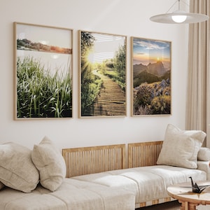 May include: Three framed landscape photographs with a nature theme. The first image shows a grassy field with a lake in the background. The second image shows a wooden walkway through a forest with a sunbeam shining through the trees. The third image shows a mountain range with a sunset in the background.