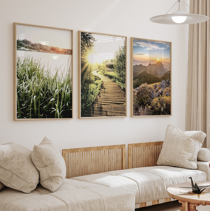 May include: Three framed landscape photographs with a nature theme. The first image shows a grassy field with a lake in the background. The second image shows a wooden walkway through a forest with a sunbeam shining through the trees. The third image shows a mountain range with a sunset in the background.