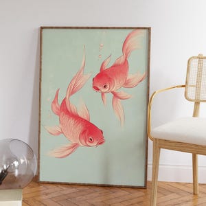 May include: A framed art print featuring two red goldfish swimming against a light teal background. The fish have detailed scales and flowing fins. The artwork is displayed in a room with a wooden floor and a chair.