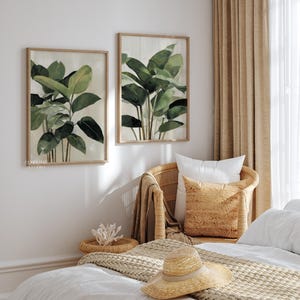 Puede incluir: Dos impresiones bot&aacute;nicas enmarcadas con pinturas de acuarela de exuberantes hojas verdes. Las impresiones est&aacute;n sobre una silla de mimbre con almohadas y un sombrero de paja en una cama, creando una est&eacute;tica serena y natural.