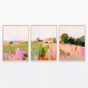 May include: A set of three framed wall art prints featuring a continuous landscape painting. The artwork displays a rural scene with a white farmhouse, green fields, and vibrant pink wildflowers under a soft, pale sky, all encased in light wood frames.
