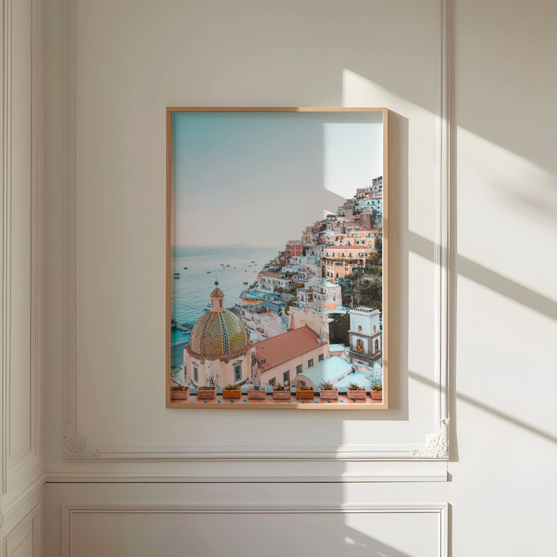 May include: A colorful photograph of a coastal town with a large, domed church building in the foreground. The town is built on a hillside overlooking the ocean. The sky is blue and the water is a light blue.