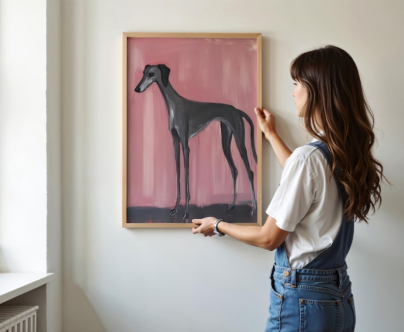Puede incluir: Obra de arte enmarcada con una ilustraci&oacute;n de un galgo. El perro est&aacute; representado en gris sobre un fondo rosa. La obra est&aacute; encerrada en un marco de madera marr&oacute;n claro, proporcionando una est&eacute;tica cl&aacute;sica.