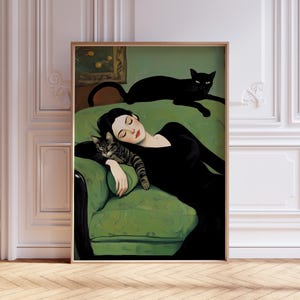 May include: A framed art print depicts a woman in a black dress reclining on a green sofa with two cats. One cat is striped and resting on the woman's arm, while the other is black and lounging on the sofa's back. The artwork has a vintage aesthetic.